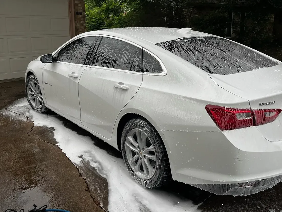 White Chevrolet Malibu covered in foam during a mobile hand wash in a driveway